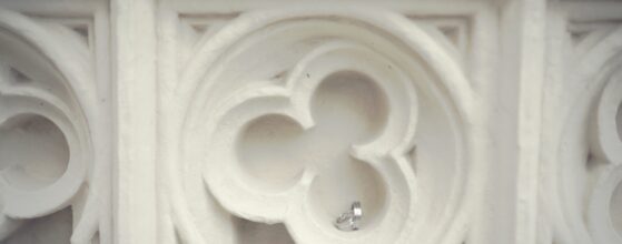 Hochzeitringe von Doris und Lucas liegen auf einem eleganten weißen Ornament-Detail der Schloss Hernstein Architektur – Nahaufnahme Hochzeitsvideograf Schloss Hernstein Niederösterreich Austria