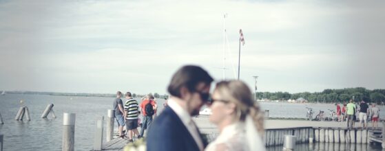 Ines und Markus umarmen sich auf einem Holzsteg am See beim Schloss Halbturn, mit Wasser und Himmel im Hintergrund – romantische Hochzeitsfoto Hochzeitsvideograf Seehochzeit Schloss Halbturn Burgenland