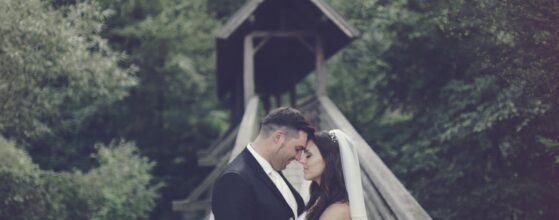 Jeannine und Manuel küssen sich romantisch vor der historischen Krainerhütte-Kapelle in Baden bei Wien, umgeben von grüner Natur und Waldkulisse