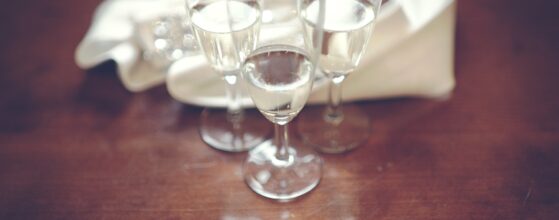 Drei elegante Champagnergläser stehen auf einem dunklen Holztisch beim Schloss Hernstein, mit unscharfem Brautpaar im Hintergrund