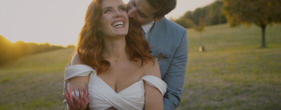 Kathi und Sebastian lächeln sich auf einer Wiese im Sonnenuntergang an, im Hintergrund der Wienerwald.